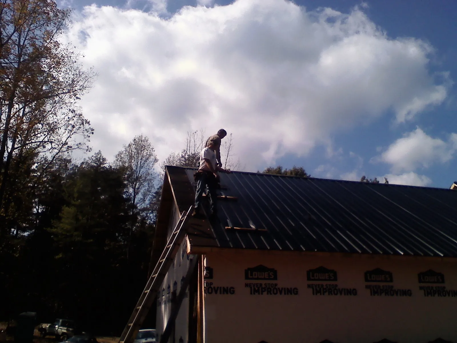 Roofer fastening dark metal panels high against a cloudy sky, from a Roof Inspection job in Newman Lake