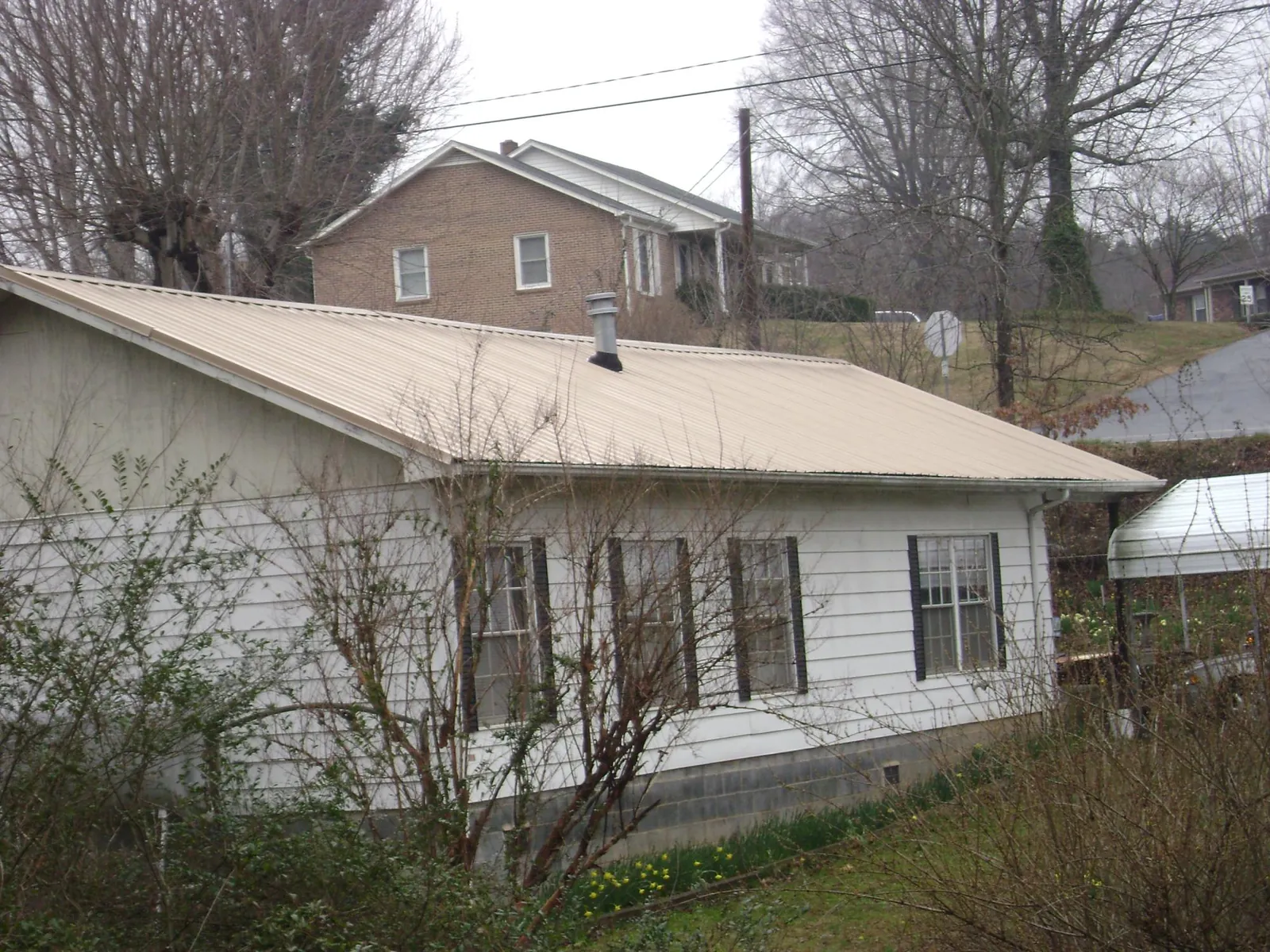 Tan metal roof on a white sided house set into a hillside — Commercial Roofing by Roofing Brothers in Newman Lake
